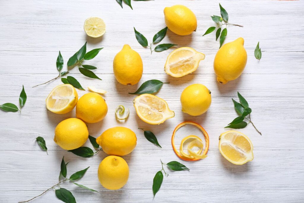 Sopra una superficie in legno bianco, alcuni limoni sia interi che a metà