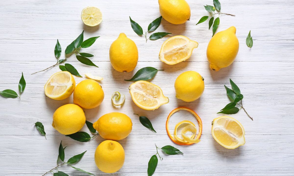 Sopra una superficie in legno bianco, alcuni limoni sia interi che a metà