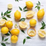 Sopra una superficie in legno bianco, alcuni limoni sia interi che a metà
