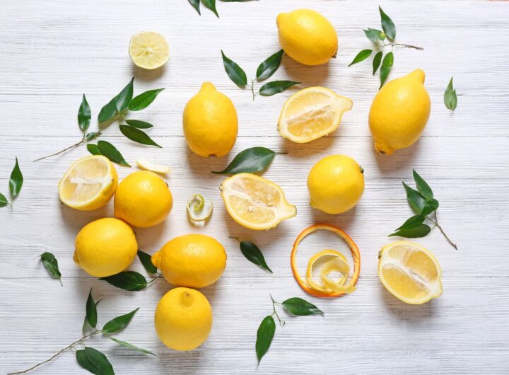 Sopra una superficie in legno bianco, alcuni limoni sia interi che a metà