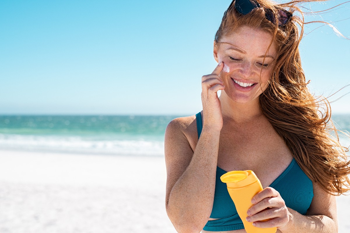 Giovane donna applica la crema solare sul viso durante una giornata al mare.