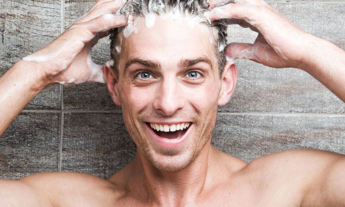 Ragazzo che si applica lo shampoo sui capelli sotto la doccia.