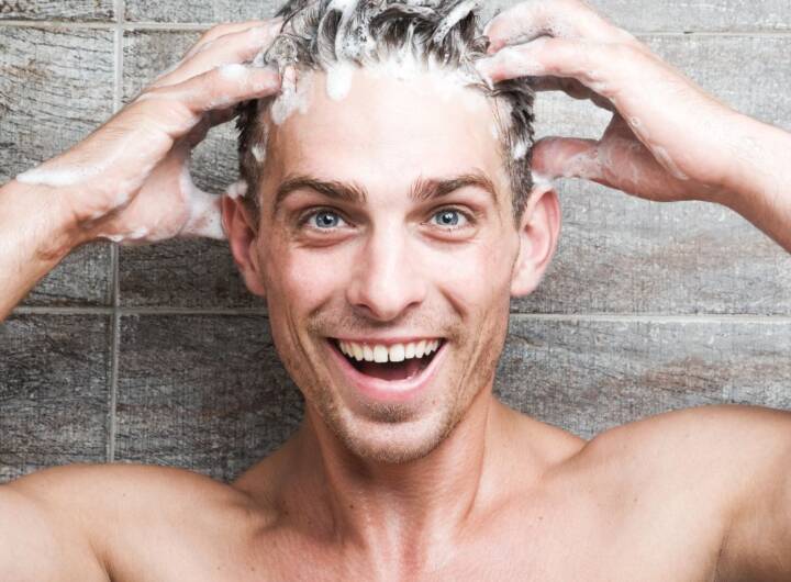 Ragazzo che si applica lo shampoo sui capelli sotto la doccia.